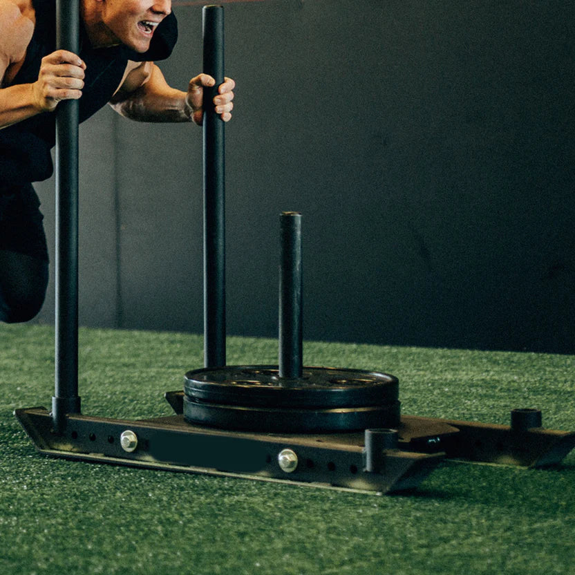 Person using a weightlifting platform with weights on a green floor.