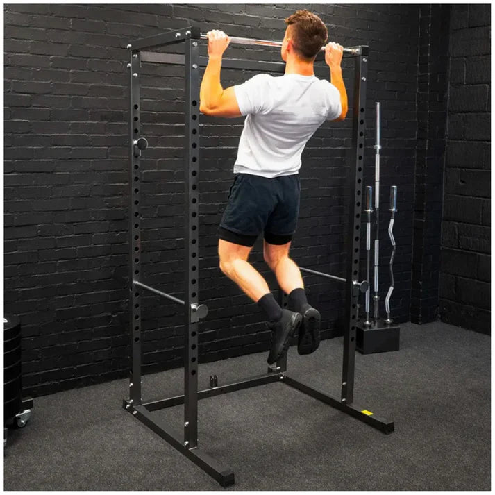 Person using a pull-up bar on a black metal power rack against a black brick wall.