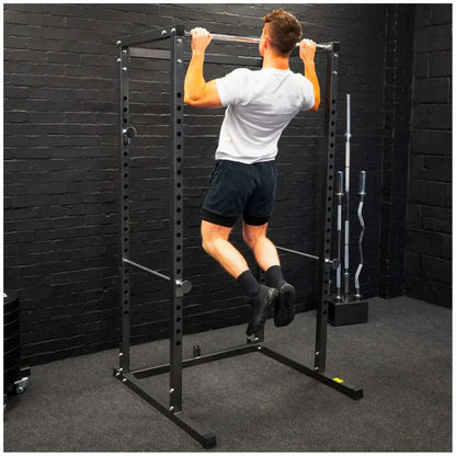 Person using a pull-up bar on a black metal power rack against a black brick wall.